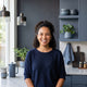 A professional portrait of a smiling woman in a modern, stylish kitchen with charcoal and blue accents.
